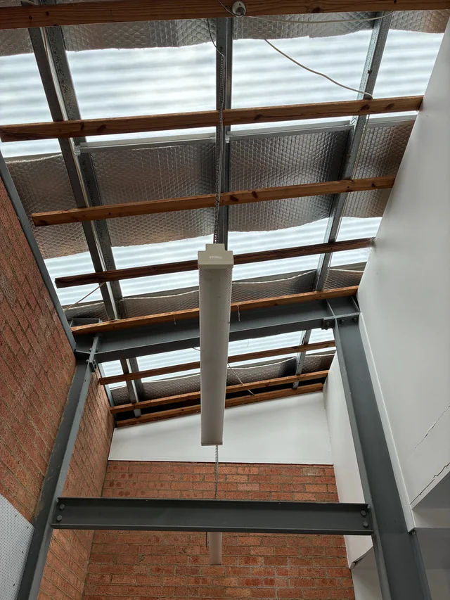 Translucent roof sheets and insulation above steel supports and timber battens, viewed from inside a brick building.