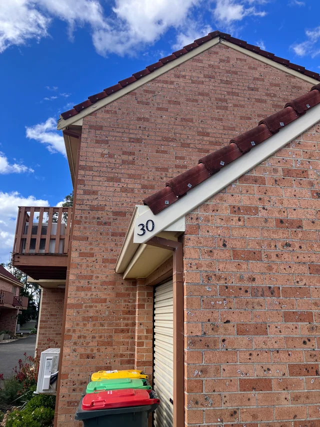 Brick home exterior showing tiled roof edges and white eaves against a blue sky.